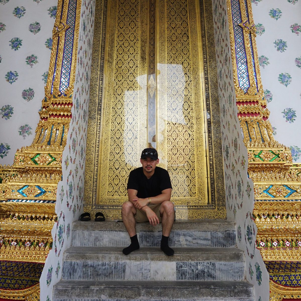 Vang sitting on the steps of an ornate gold temple doorway in Bangkok